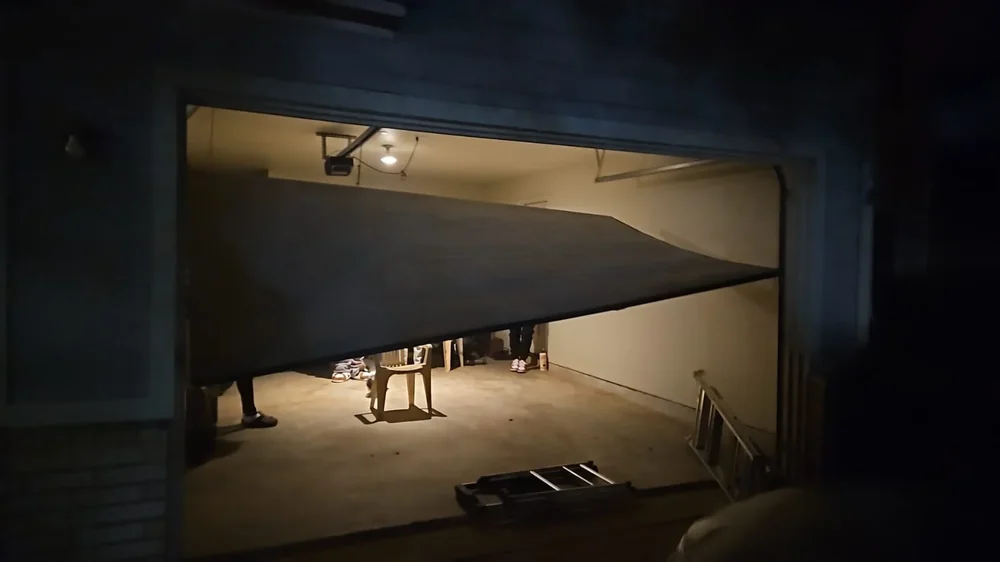 Damaged garage door hanging diagonally across opening at night