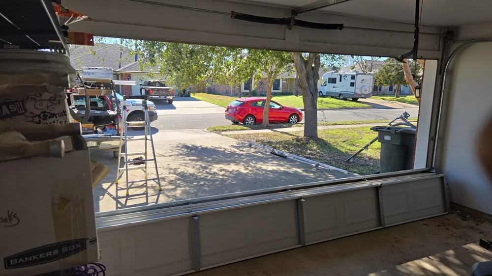 Wide inside-out view of partially installed garage door and driveway