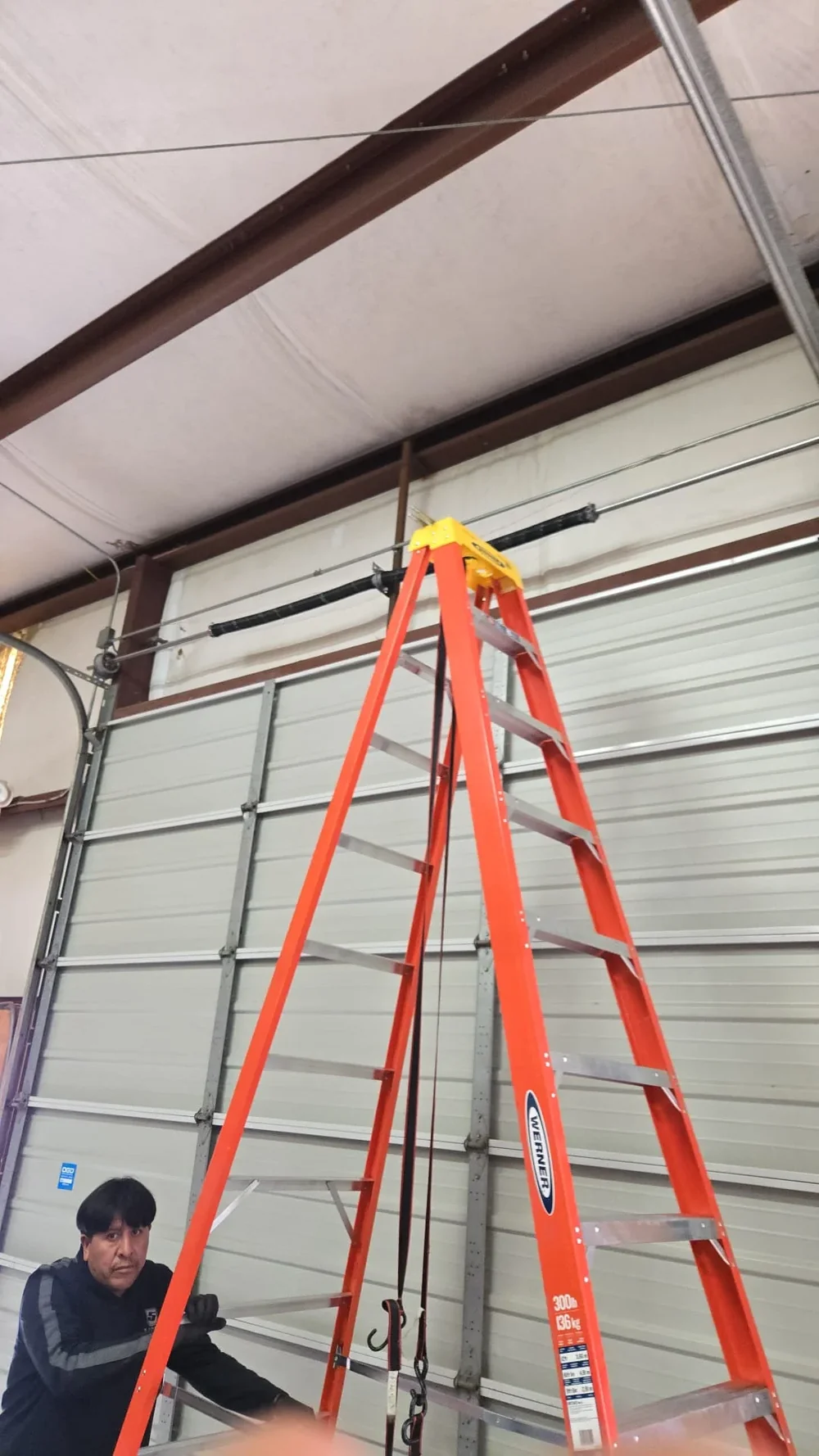 Technician servicing a garage door beneath a ladder